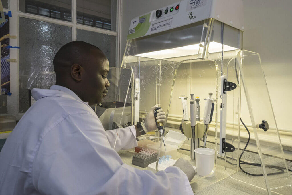 A laboratory technologist sits at a desk and interacts with lab samples