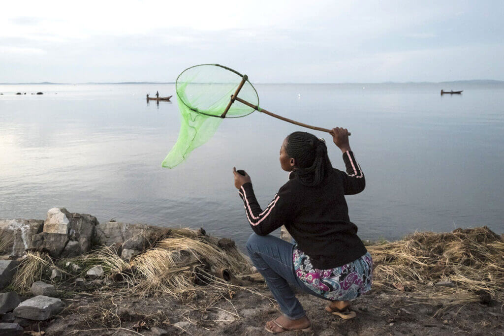 A womanholds a net and holds it above a lake for swarming purposes.