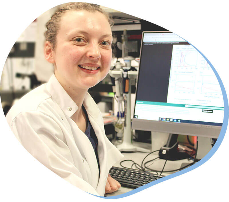 Photo of Katie Willis, she sits in front of a comupter and smiles at the camera