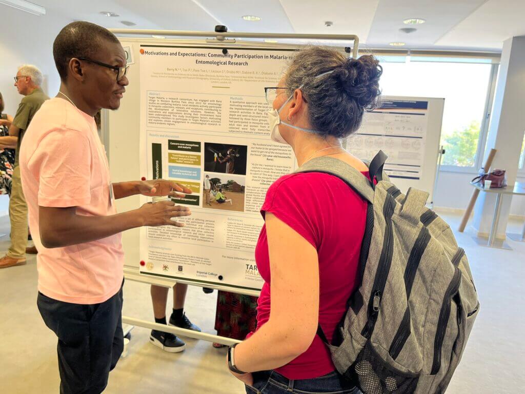 Nourou Barry stands presents a display board of information to a woman at an event.