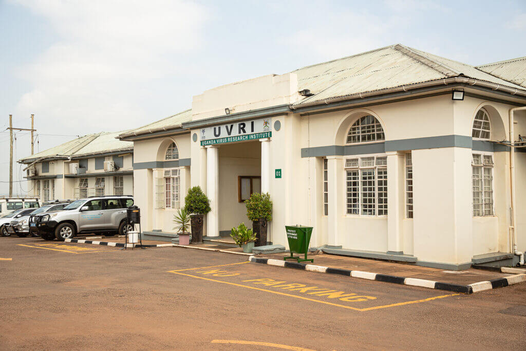 Photo of the UVRI building. The building is painted a cream colour and has arched windoes. There is a parking lot outside.