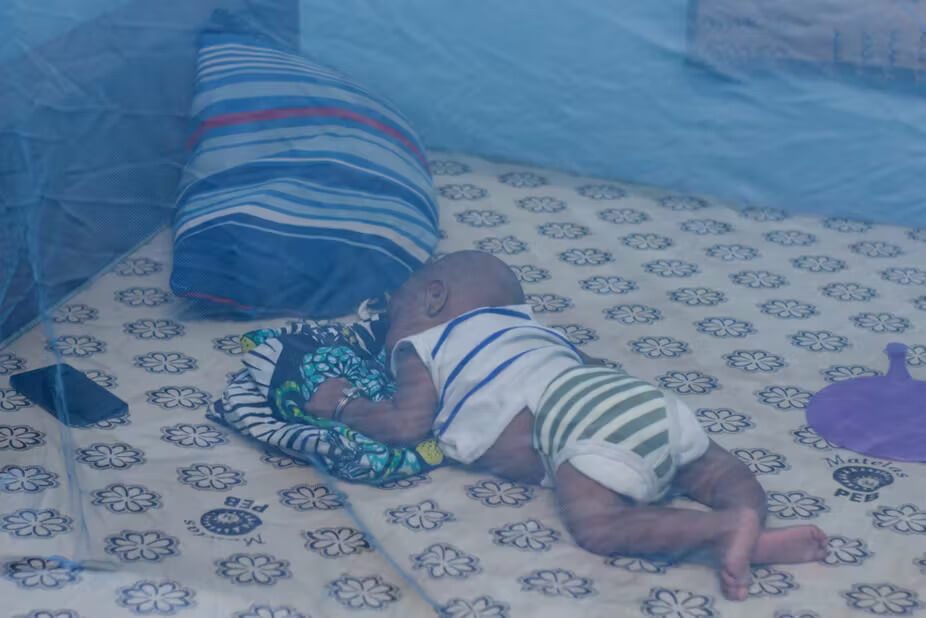 A baby sleeps under the cover of a mosquito net